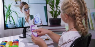在网络教育中，女孩在学习学校课程数学的过程中，用电脑在桌子旁向女老师展示有数字的卡片