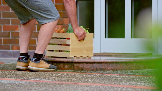 一个男人带着一个装着新鲜农产品的木箱站在家门口