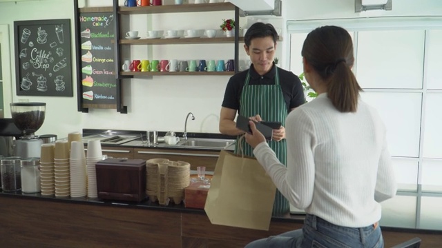 女服务员在咖啡馆柜台为顾客送咖啡和纸袋。