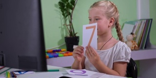 一名在家接受教育的小学生的肖像，在流感期间，一名手持卡片的女学生在房间里通过电脑观看在线数学课