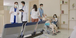 跟踪缓慢:两名医生在医院大堂或走廊与忙碌的护士、坐轮椅的老年患者、病人、带着医用口罩在接待处等候的亲属一起讨论和交谈。