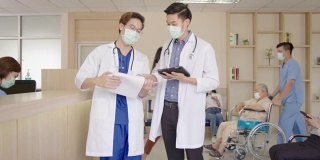放大镜头:两名医生在医院大堂或走廊里与忙碌的护士、坐轮椅的老年患者、病人、带着医用口罩在接待处等候的亲属一起讨论和交谈。