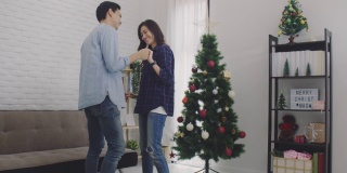 在圣诞树的背景下，年轻的亚洲情侣情侣在圣诞节和快乐的新年节日一起跳舞。圣诞节庆祝情人的概念。4 k慢动作。