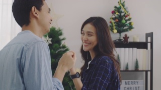 在圣诞树的背景下，年轻的亚洲情侣情侣在圣诞节和快乐的新年节日一起跳舞。圣诞节庆祝情人的概念。4 k慢动作。视频素材模板下载