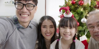 透过手机屏幕，快乐的亚洲家庭在隔离区圣诞快乐，享受自拍群视频通话，一起坐在家里公寓，享受与圣诞树的休闲时光。