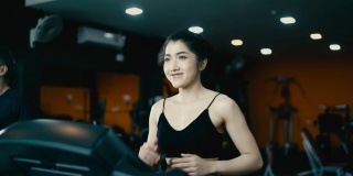 一位迷人的亚洲女子穿着黑色连衣裙在健身房里的跑步机上锻炼。