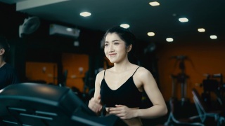 一位迷人的亚洲女子穿着黑色连衣裙在健身房里的跑步机上锻炼。视频素材模板下载
