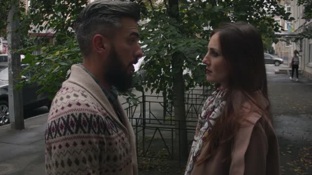 在一个阴天的秋天，一名中年男子和一名妇女在城市的街道上咒骂。一个穿毛衣的男人和一个穿外套的女人在城市的街道上争吵，解决问题。