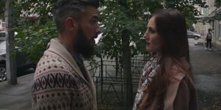 在一个阴天的秋天，一名中年男子和一名妇女在城市的街道上咒骂。一个穿毛衣的男人和一个穿外套的女人在城市的街道上争吵，解决问题。