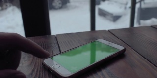 在咖啡馆的木桌上，一名男子用绿色屏幕的手机打字。