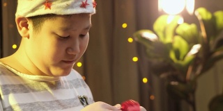 亚洲男孩戴着圣诞帽，在家里打开圣诞礼盒与惊喜。