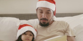一位亚洲父亲和他的女儿在卧室里读圣诞童话。