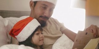 一位亚洲父亲和他的女儿在卧室里读圣诞童话。