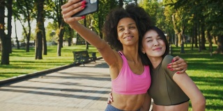 开心的女性朋友们在公园散步时用智能手机自拍，跟踪拍摄
