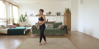 一个年轻的印度女芭蕾舞演员在家里训练，在明亮舒适的房间里做动感运动，穿着黑色上衣和打底裤。运动理念健康生活