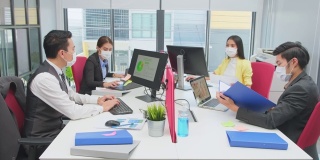 亚洲团队的商务人士在办公室工作与新的正常的社会距离的生活理念。男性和女性在一起时佩戴防护口罩，保持距离，防止冠状病毒感染