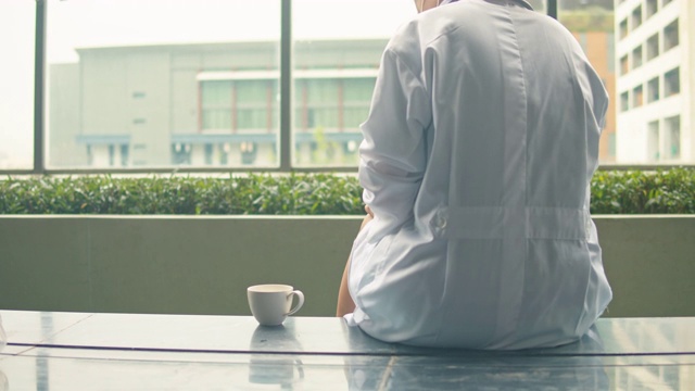 女医生站在窗口边用手机边喝热咖啡