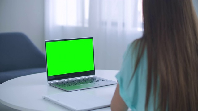 女孩在笔记本电脑上做笔记绿色模拟屏幕。女孩在网上学习电脑