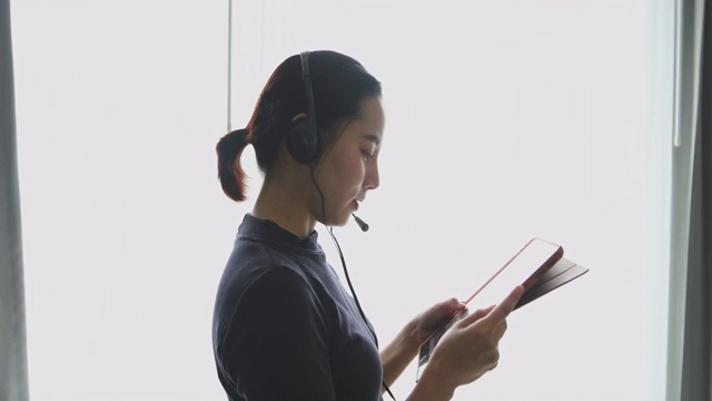 亚洲女性戴着耳机，用数字平板电脑视频开会，在家开会