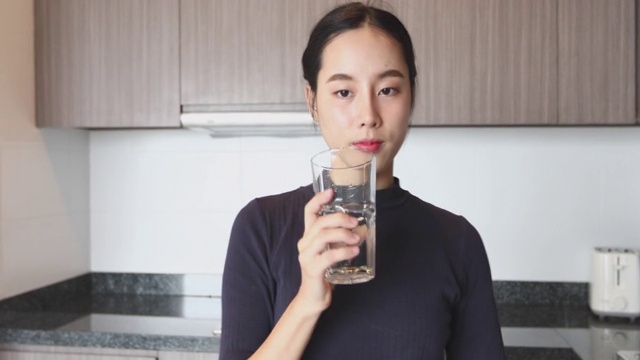 用玻璃杯喝水的亚洲女人。