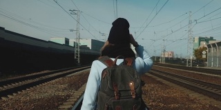 女孩Sunny day背着背包走在铁轨上。