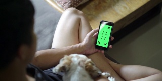 一个坐在狗旁边的人在家里使用和看着智能手机的绿色屏幕