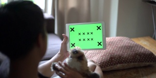 在家里，一个坐在狗旁边的人在用绿色屏幕看数字平板电脑