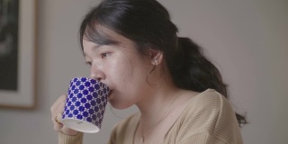 年轻女子坐在白色的床上，喝咖啡在家里的早晨。