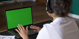 一个年轻的印度女人用一台绿屏笔记本电脑与客户交流的特写，在线电话会议，与人培训，使用电脑。众议院椅子上明亮的房间