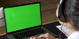 一个年轻的印度女人用一台绿屏笔记本电脑与客户交流的特写，在线电话会议，与人培训，使用电脑。众议院椅子上明亮的房间