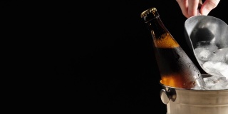 新鲜的啤酒。在黑色的背景下，用勺子将冰冷的真冰倒入棕色瓶子里的美味精酿啤酒中。冰镇新鲜啤酒与水滴。准备饮料。4 k