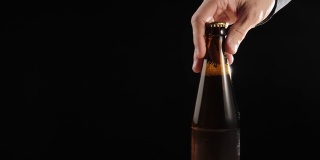 新鲜的啤酒。Hand把一个棕色的瓶子和美味的精酿啤酒放在一张黑色背景的木桌上。冰镇新鲜啤酒与水滴。准备饮料。4 k