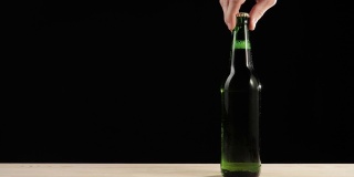 新鲜的啤酒。Hand把一个绿色的瓶子和美味的精酿啤酒放在一张黑色背景的木桌上。冰镇新鲜啤酒与水滴。准备饮料。广角镜头。4 k
