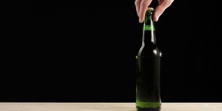 新鲜的啤酒。Hand从黑色背景的木桌上拿起一个绿色的瓶子，里面装着美味的精酿啤酒。冰镇新鲜啤酒与水滴。准备饮料。广角镜头。4 k