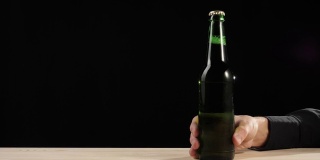 新鲜的啤酒。手拿着一瓶绿色的精酿啤酒在黑色背景的木桌上滑了进去。冰镇新鲜啤酒与水滴。准备饮料。广角镜头。4 k