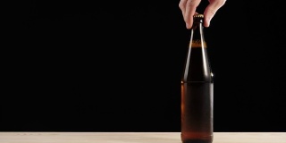 新鲜的啤酒。Hand从黑色背景的木桌上拿起一个棕色的瓶子，里面装着美味的精酿啤酒。冰镇新鲜啤酒与水滴。准备饮料。广角镜头。4 k