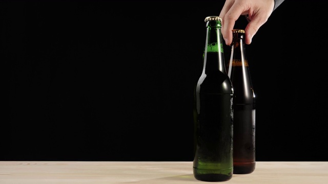 新鲜的啤酒。Hand拿着一个棕色的瓶子，里面装着美味的精酿啤酒，旁边是一个绿色的瓶子，里面装着啤酒，放在一张黑色的木桌上。冰镇新鲜啤酒与水滴。准备饮料。4 k