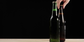 新鲜的啤酒。Hand拿着一个棕色的瓶子，里面装着美味的精酿啤酒，旁边是一个绿色的瓶子，里面装着啤酒，放在一张黑色的木桌上。冰镇新鲜啤酒与水滴。准备饮料。4 k