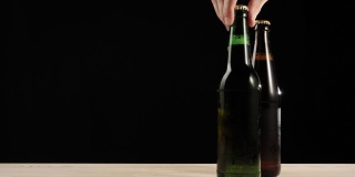 新鲜的啤酒。Hand把一个绿色的瓶子和一瓶美味的精酿啤酒放在一张黑色背景的木桌上。冰镇新鲜啤酒与水滴。准备饮料。4 k