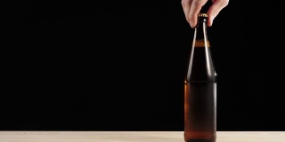 新鲜的啤酒。Hand把一个棕色的瓶子和美味的精酿啤酒放在一张黑色背景的木桌上。冰镇新鲜啤酒与水滴。准备饮料。广角镜头。4 k