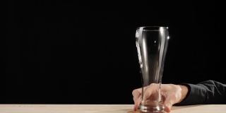 新鲜的啤酒。汉德把啤酒杯放在啤酒杯架上，放在黑色背景的木桌上。冰镇新鲜啤酒与水滴。准备饮料。4 k