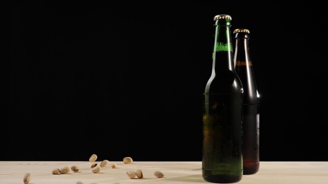新鲜的啤酒。在黑色背景的木桌上，人们把开心果扔在绿色和棕色的瓶子旁边，还有美味的精酿啤酒。冰镇新鲜啤酒与水滴。4 k