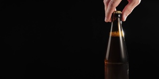 新鲜的啤酒。Hand从黑色背景的木桌上拿起一个棕色的瓶子，里面装着美味的精酿啤酒。冰镇新鲜啤酒与水滴。准备饮料。4 k