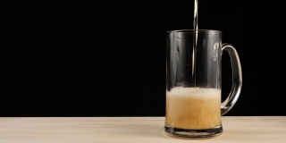 新鲜的啤酒。在黑色背景的木桌上，用啤酒杯盛满美味的手工啤酒。冰凉的新鲜啤酒，带有水滴，泡沫和泡沫。4 k
