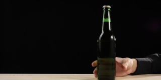 新鲜的啤酒。在黑色背景的木桌上，他拿出一瓶绿色的精酿啤酒。冰镇新鲜啤酒与水滴。准备饮料。广角镜头。4 k