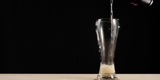 新鲜的啤酒。手把一杯美味的精酿啤酒倒在啤酒杯上，放在黑色的木桌上。冰凉的新鲜啤酒，带有水滴，泡沫和泡沫。准备饮料。4 k