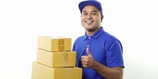 微笑的年轻亚洲快递员在蓝色制服显示大拇指举着包裹纸箱在孤立的白色背景。4 k决议。