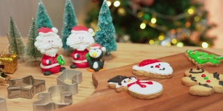 糖衣装饰的自制圣诞饼干，红鞋，雪人，姜饼，圣诞老人木制桌子上的饼干金属模具。有些饼干放在木制的盘子里，上面有黄色的圣诞礼物、圣诞树、灯和装饰品。