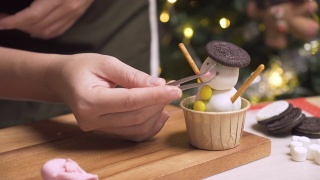 特写镜头:为冬天的传统节日圣诞节准备烘焙食品和甜点摊，用糖霜自制纸杯蛋糕做一个雪人，晚上用镊子在厨房里用巧克力装饰眼睛。视频素材模板下载
