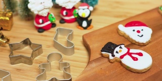 直接上方小车视图:糖霜装饰的自制圣诞饼干，红鞋，雪人，姜饼，圣诞老人木制桌子上的饼干金属模具。一些饼干在木制的盘子上有黄色的圣诞礼物，圣诞树装饰。